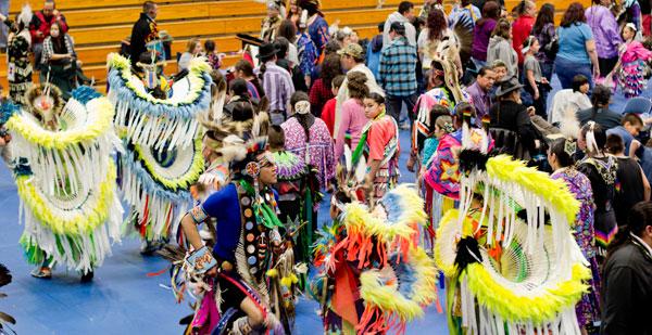 Spectators at a Pow Wow leave the stands to join dancers during an Intertribal song, during which everyone is invited to dance around the drum circles. Dancers would typically move clockwise around the different drum circles gathered in the center of the floor.