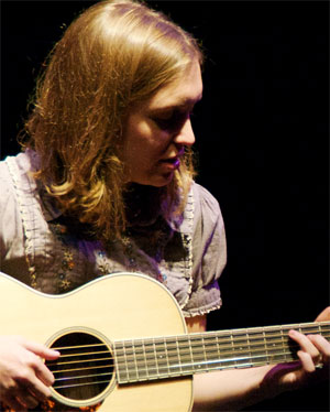 Whitney Mann strumming her guitar at the Broom Street Theater.