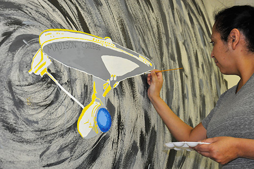 Raquel Manning paints a section of the new mural on the wall of the cafetaria.