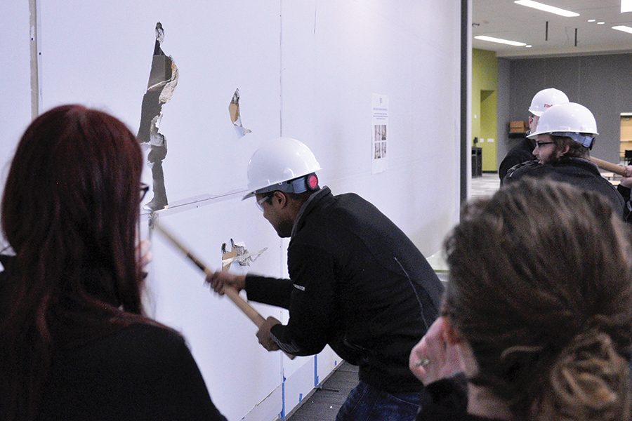 Meshan Adams, a member of the Madison College Student Senate, takes a swing with a sledge hammer at the temporary wall that separated the completed cafeteria seating area from the section that was still under construction during a ceremony on Dec. 21.