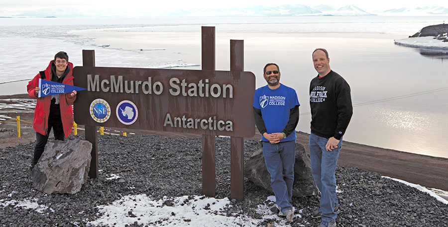 Madison College instructors Andy Kurth, right, and Matthew Lazzara, center, pose for a photograph wearing Madison College shirts at the marking the McMurdo Station in Antarctica.