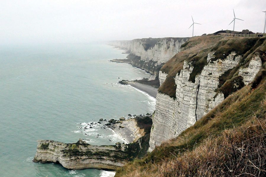 Wind turbines turn atoo a bluff overlooking the sea near Normandy, France