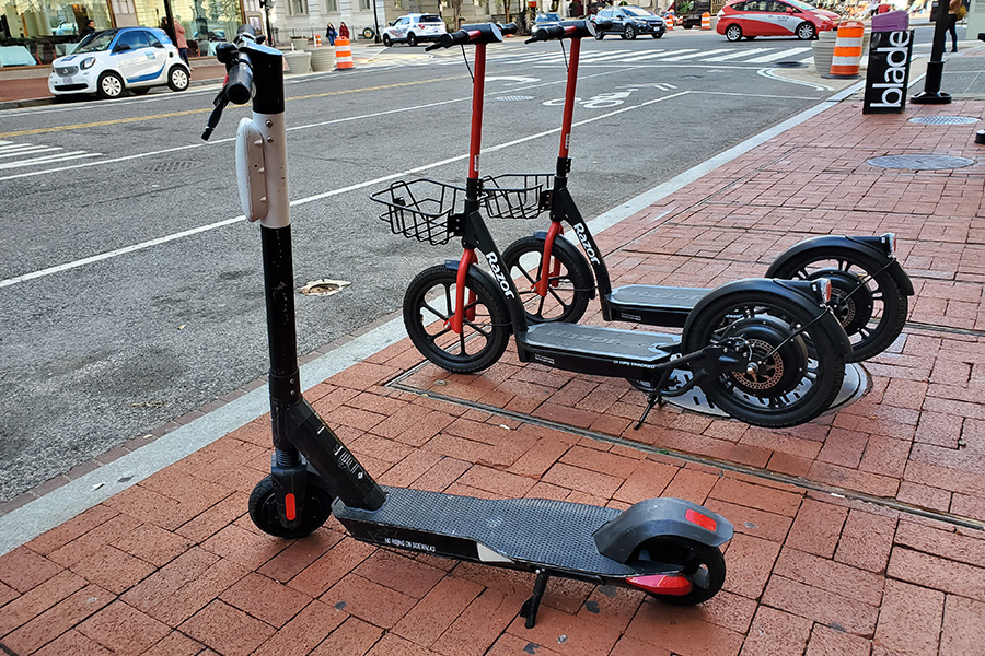 A Bird and two Razor electric scooters rest on a walkway in Washington, D.C., waiting for riders.