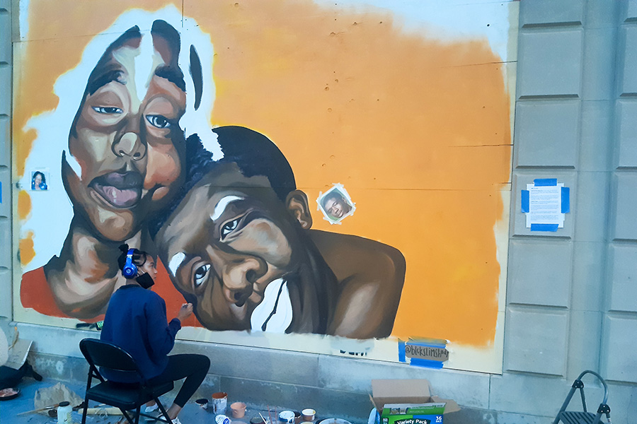 Artist Shiloah Symone Coley while working on the mural which now stands on N. Fairchild St at the side of the Overture Galleries building. Her art is inspired by Aiyana Mo’Nay Stanley and Cameron Tillman who as children were murdered by police forces and stories went untold.