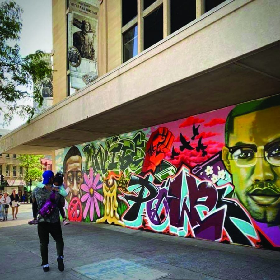 Artist Tony Catteruccia and his daughter walk past one of the murals he painted downtown Madison this summer.