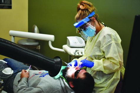 Second year dental hygienist student Dallas Ziegler cleans the teeth of Brian Uploff while using the extra-oral vacuum as a COVID-19 preventative measure that has been put into place this year.