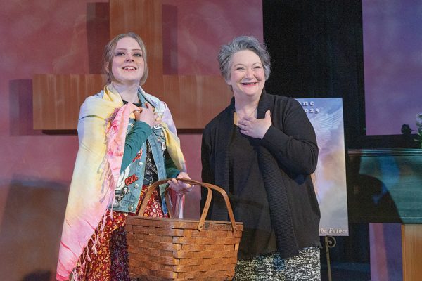 Photo of two actresses looking out to the audience, one holding a picnic basket.