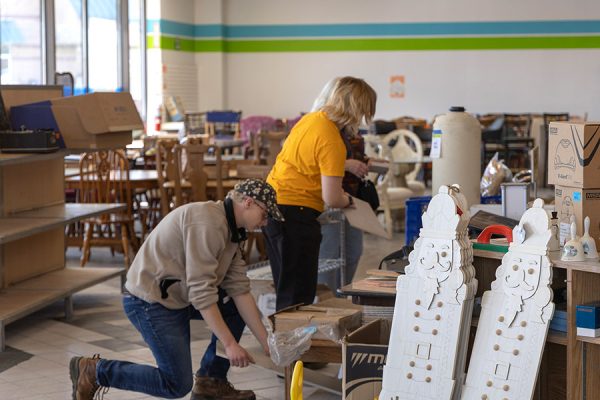 A man an a woman arrange decorative items for sale on tables in a store.