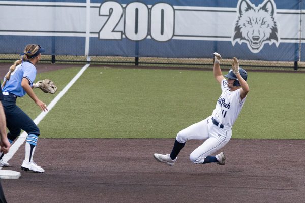A baserunner slides in as the third baseman waits for the throw.