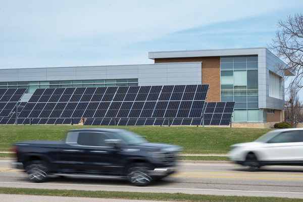 A truck and a car ride past solar panels that line the roadside near the Madison College Protective Services Building.