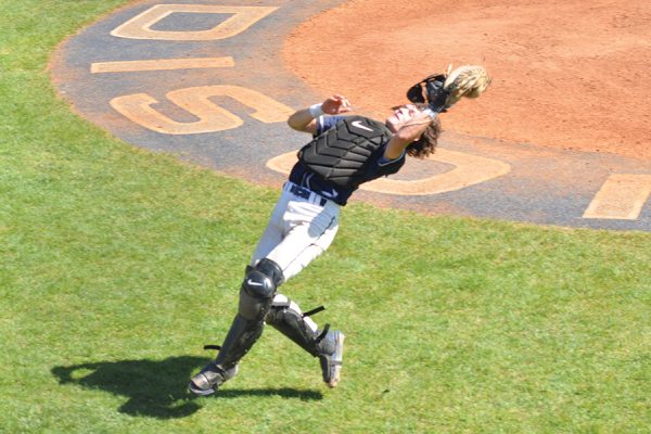 A catcher leans back and reaches up to catch a foul ball.