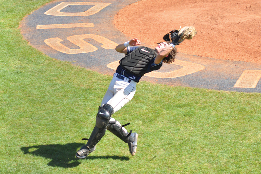 A catcher leans back and reaches up to catch a foul ball.