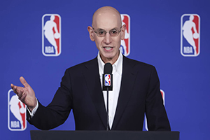 A man speaks at a podium with the NBA logo on the back wall.