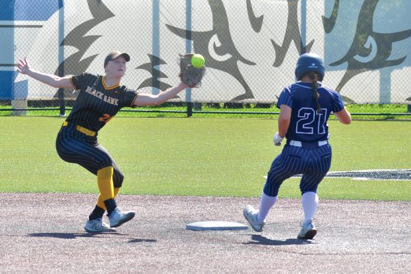 A softball base runner goes in standing at second base as the shortstop catches the ball.