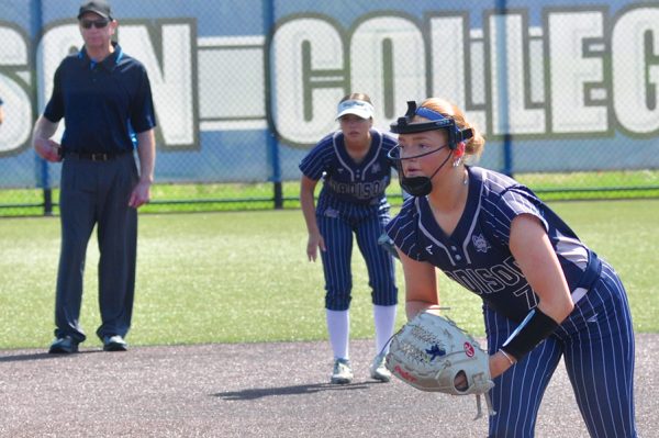 A softball pitcher leans forward with her glove in hand as she looks toward home plate.